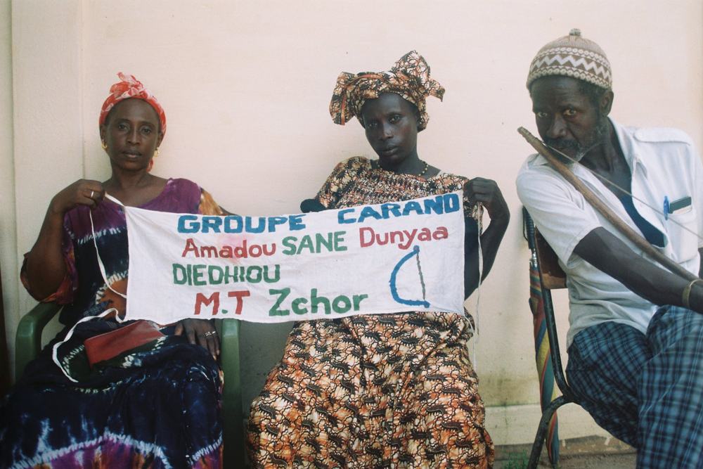Three people holding a banner reading Groupe Carand, Amadou Sane