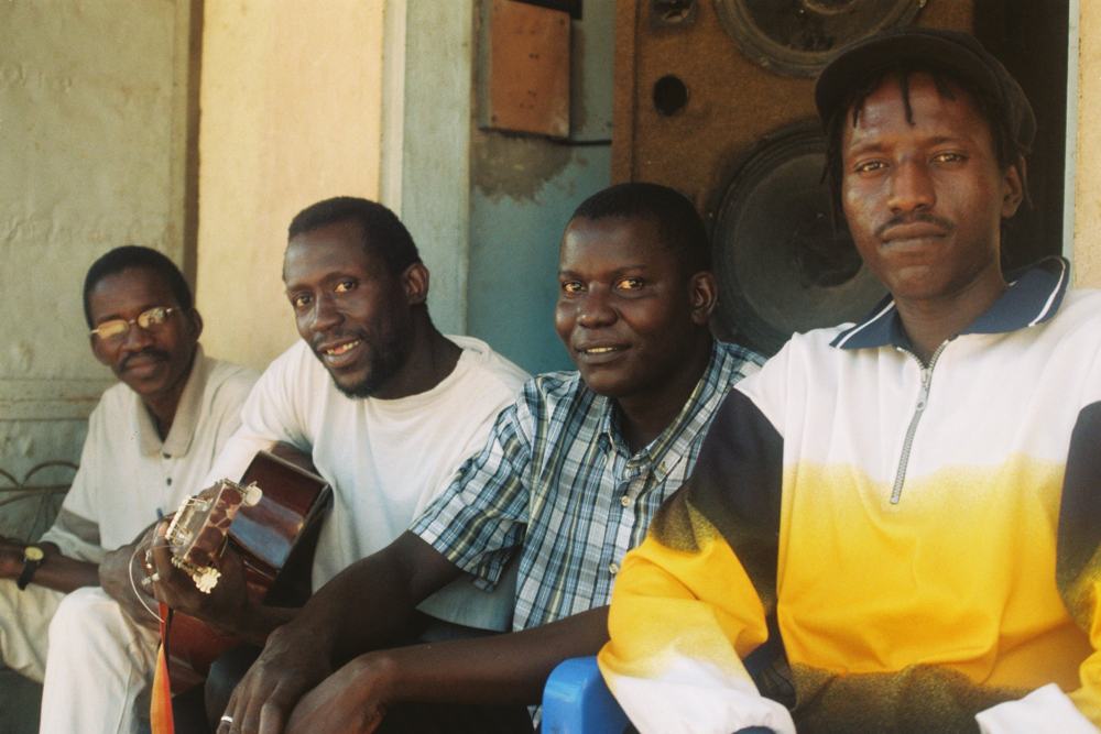 Four men sitting together, one holding a guitar